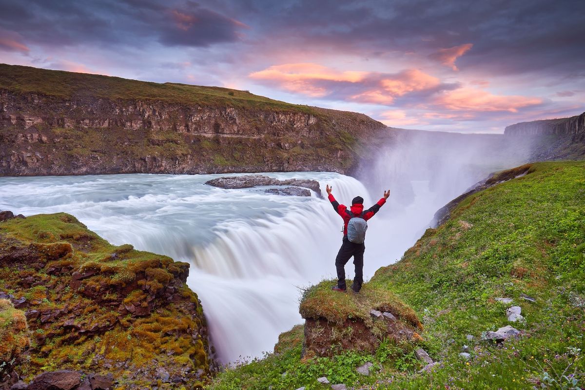 A visitor with arms raised at Gullfoss in low evening sun