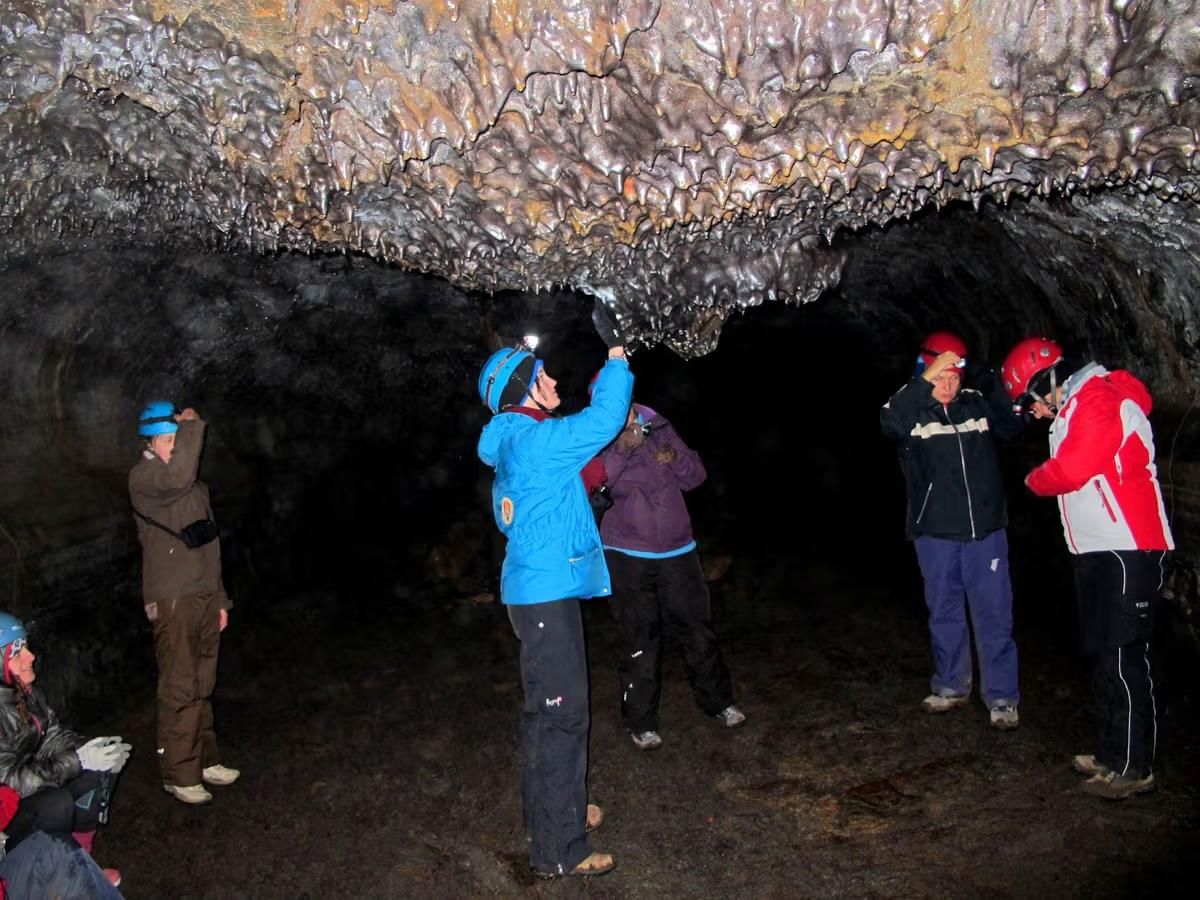 A guided group walking through the Leidarendi lava tube cave wearing helmets and headlamps