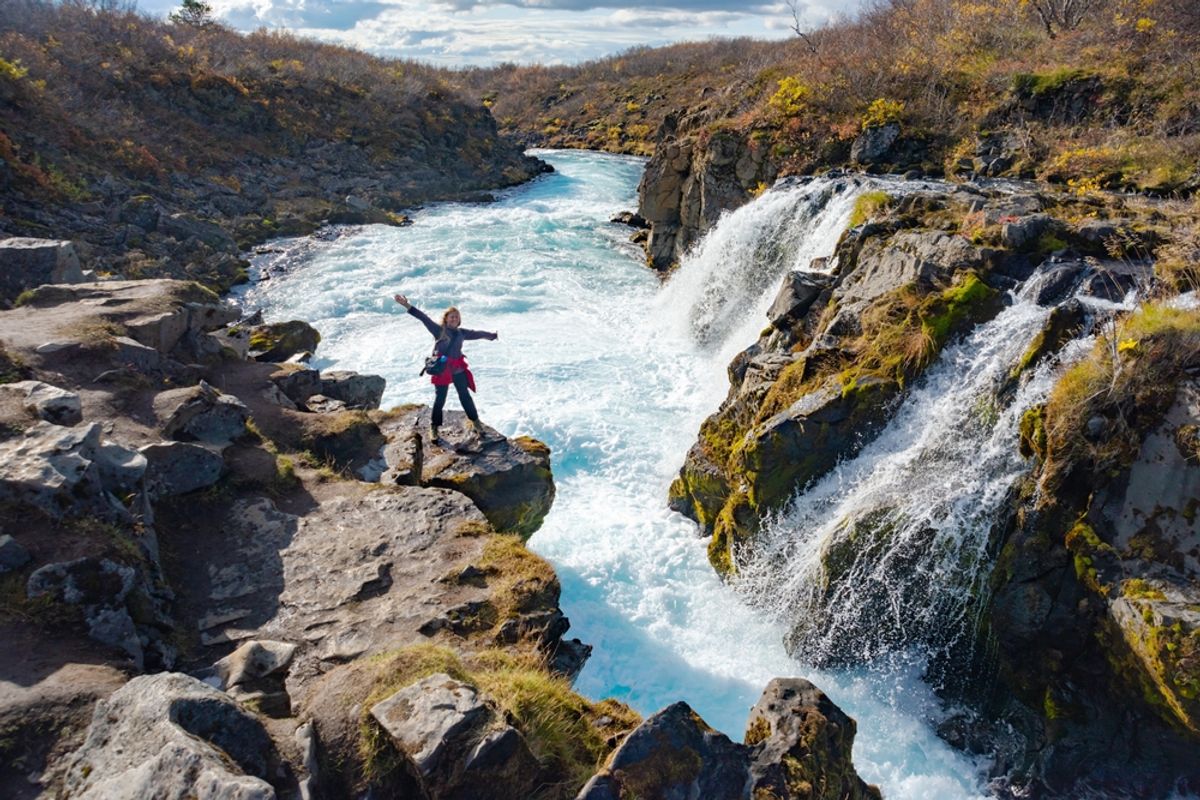 An adventurer standing triumphantly near the stunning Brúarfoss Waterfall in Iceland