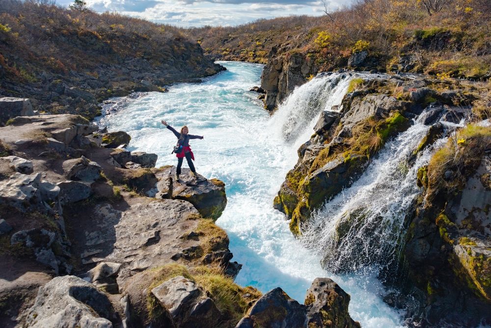 An adventurer standing triumphantly near the stunning Brúarfoss Waterfall in Iceland