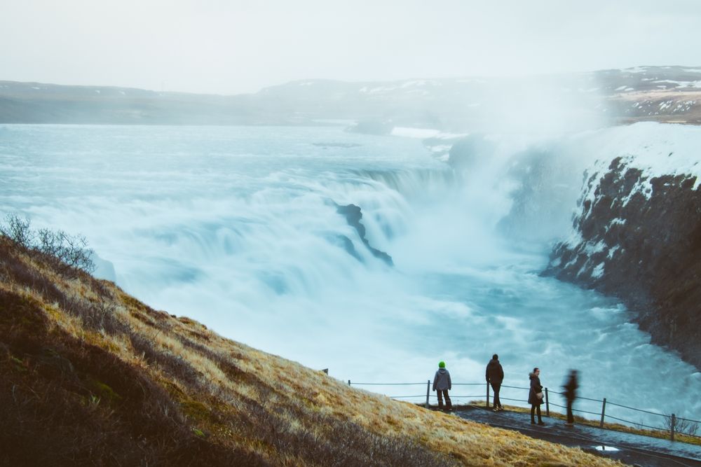 Tourists at Gullfoss Waterfall, Iceland, surrounded by snow and ice under a purple sunset sky