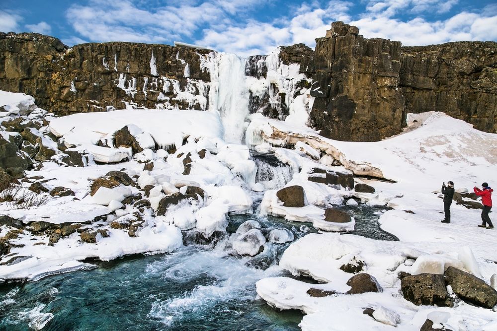 Öxarárfoss frozen in winter with visitors photographing from the boardwalk