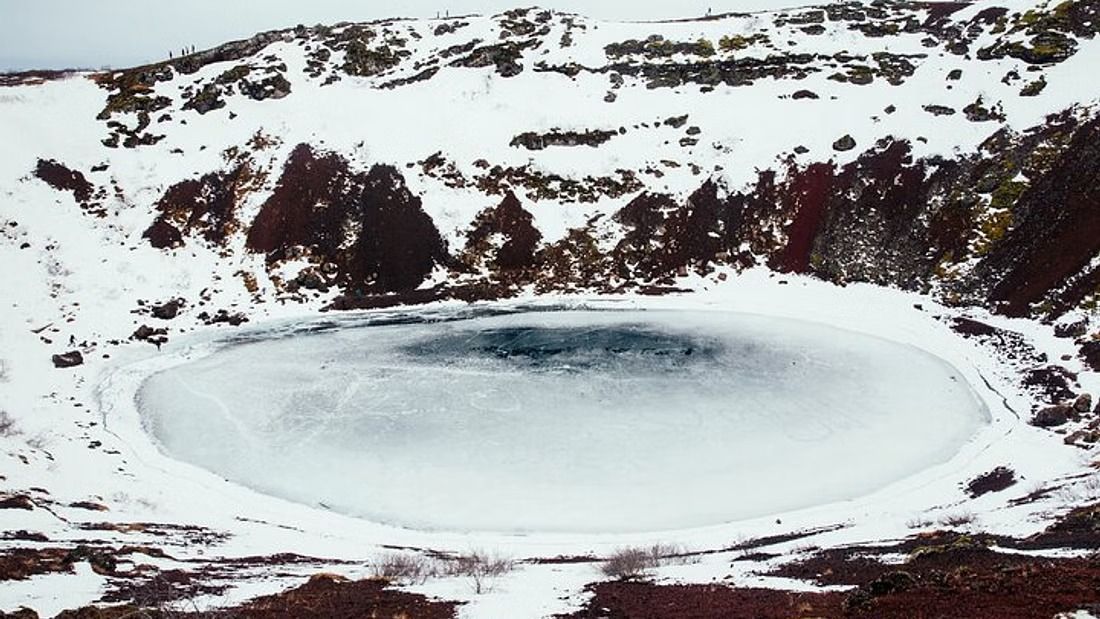 The rim of Kerið crater covered in snow above the frozen crater lake