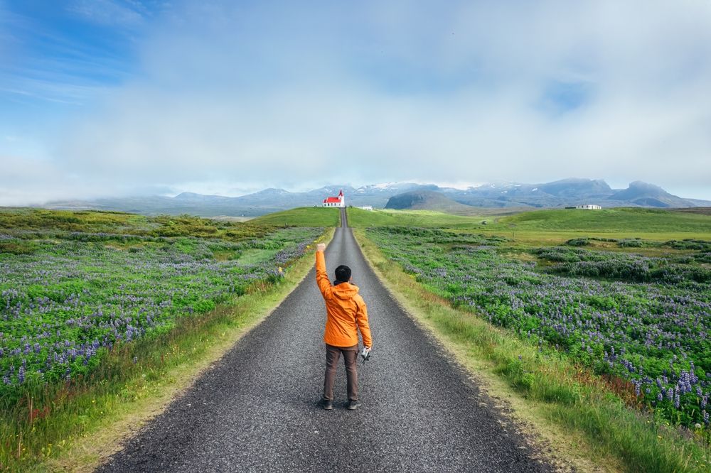 A young Asian man standing on a road near Ingjaldshólskirkja church on a hill