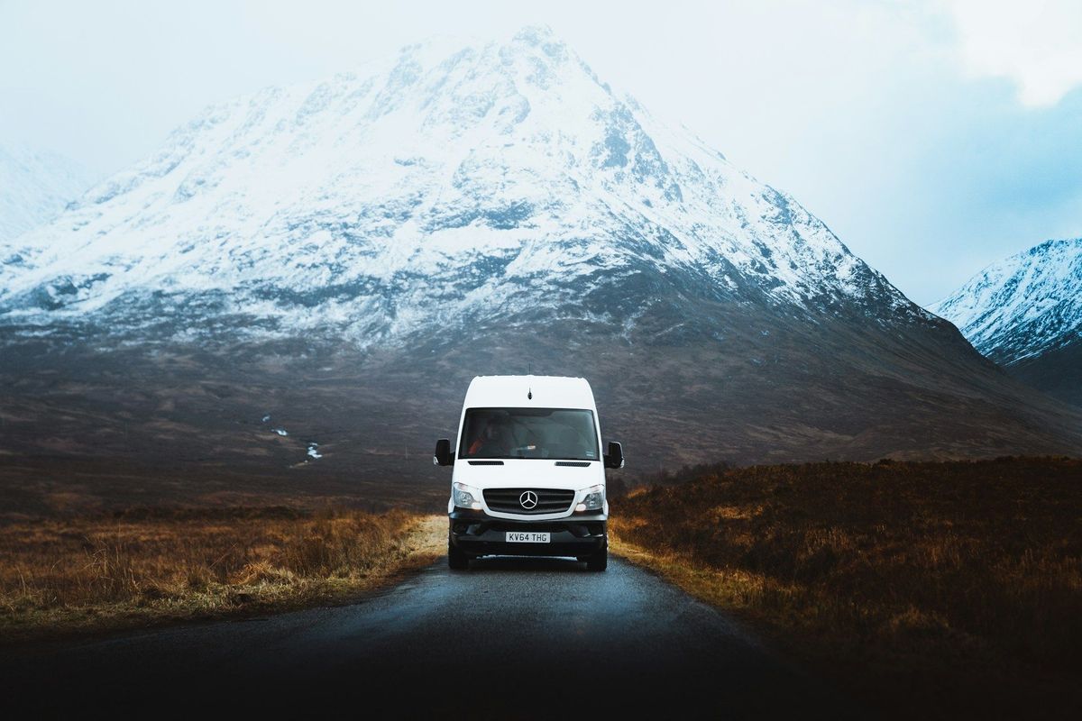 A campervan driving a paved Icelandic road with snow-covered mountains behind it