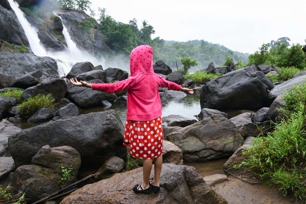 A child standing on a rock with arms outstretched, enjoying the freedom while watching a splashing waterfall
