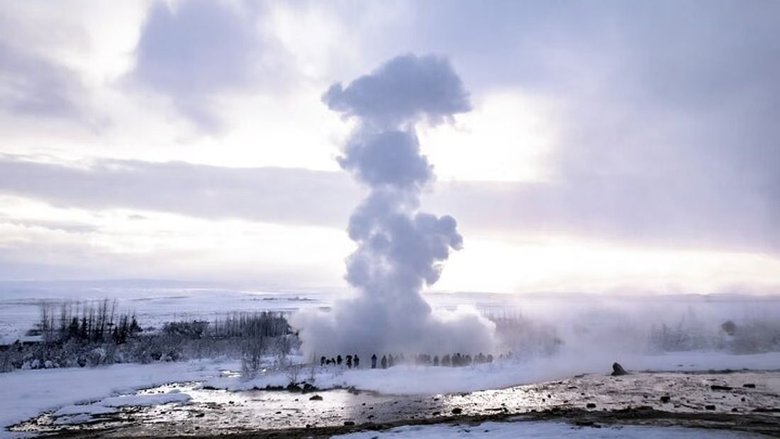 Strokkur erupting in winter with snow on the ground and visitors in heavy coats