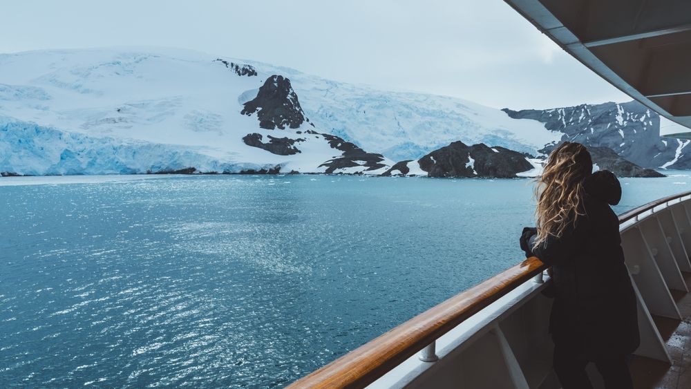 A cruise ship passenger looking out at a glacier fjord