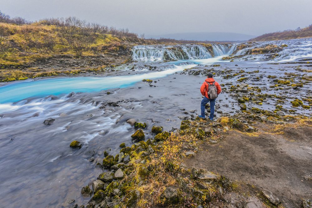 A person standing beside the blue water of Bruarfoss