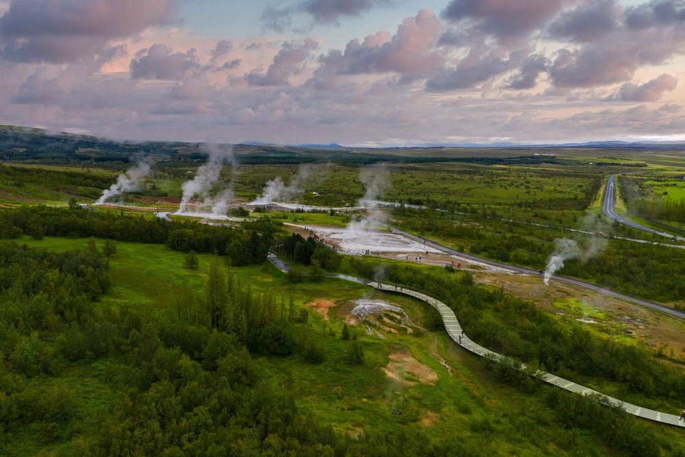 Aerial view of steam plumes, hot pools, and a winding boardwalk at the Geysir Geothermal Area in Haukadalur, Iceland