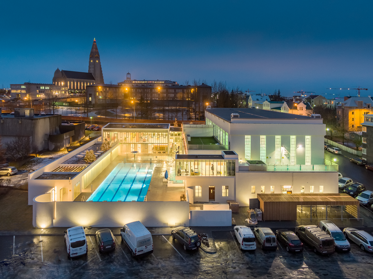 An outdoor swimming pool lit up at night in central Reykjavík, with Hallgrímskirkja church behind