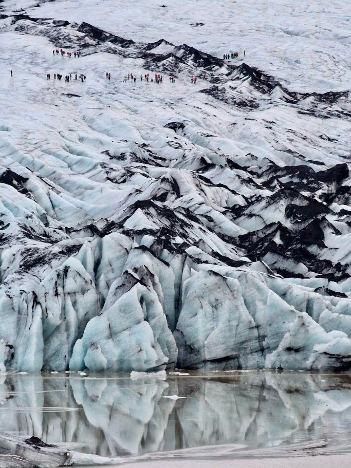 A guided group of hikers in helmets and crampons on blue glacier ice