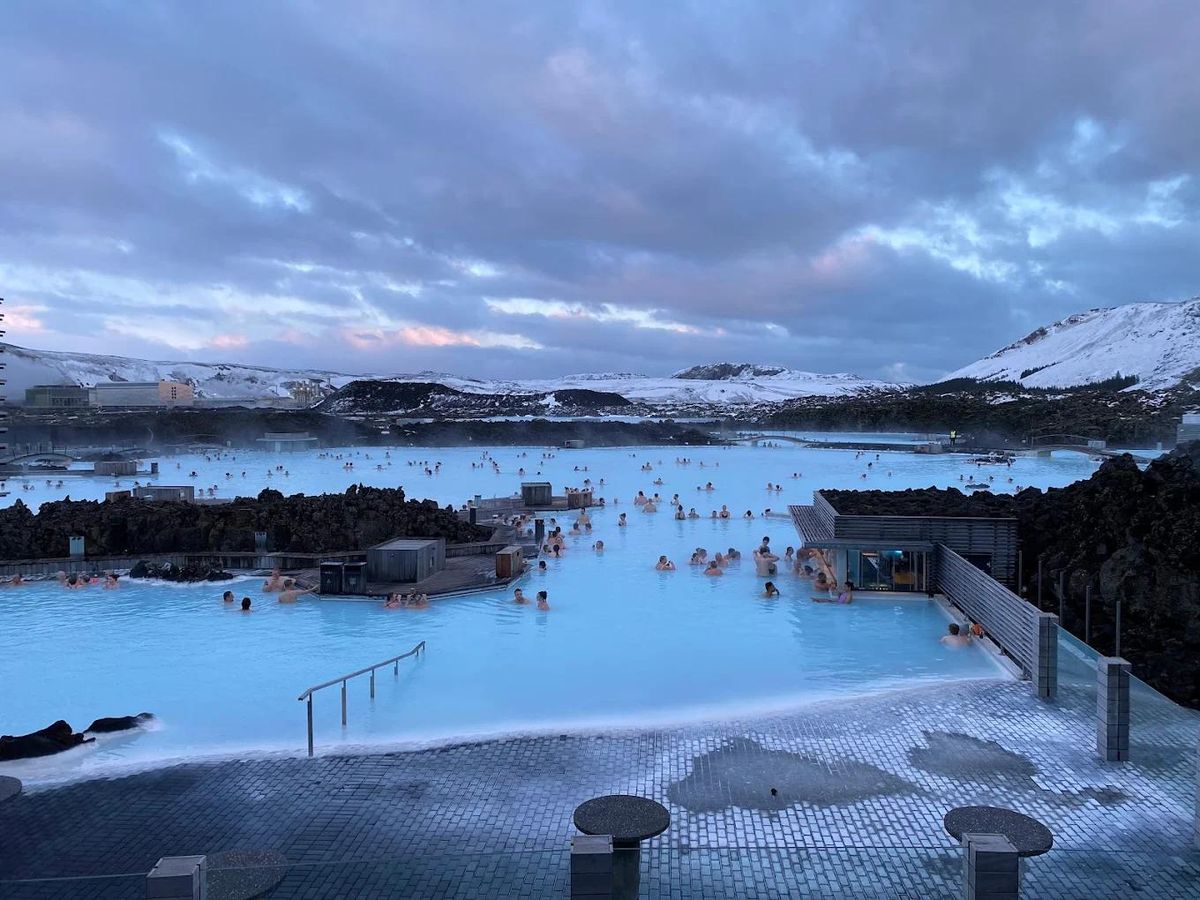 The Blue Lagoon at dusk in winter, with steam rising from milky water and snow on the hills behind