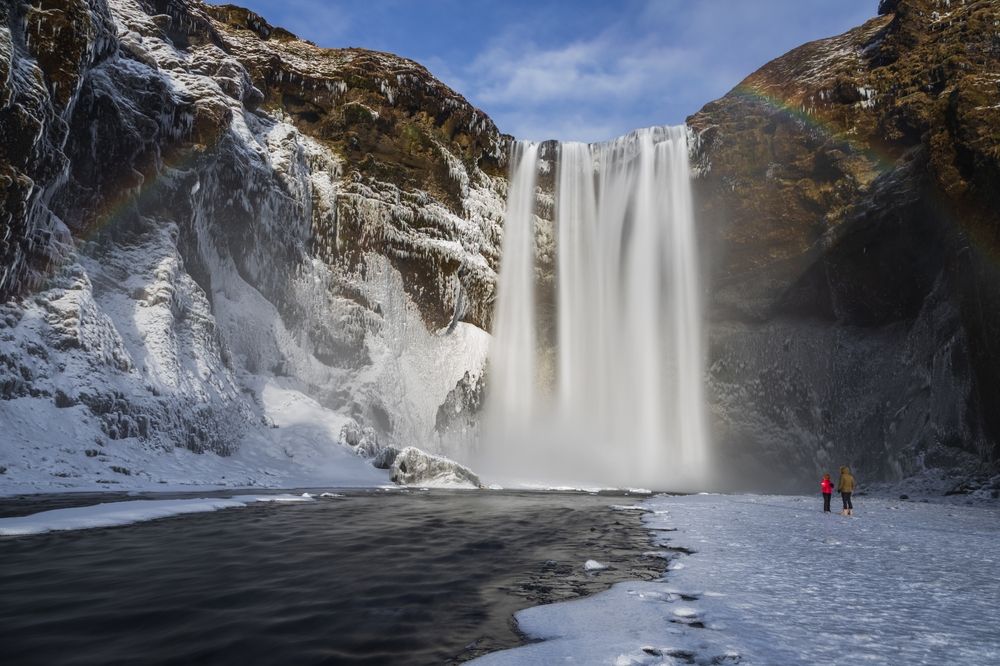Visitors stand on the frozen ground near the base of the Skogafoss waterfall
