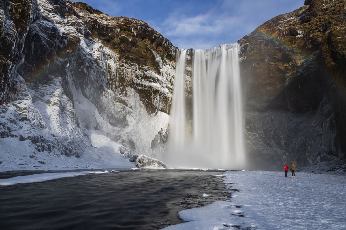 Visitors stand on the frozen ground near the base of the Skogafoss waterfall