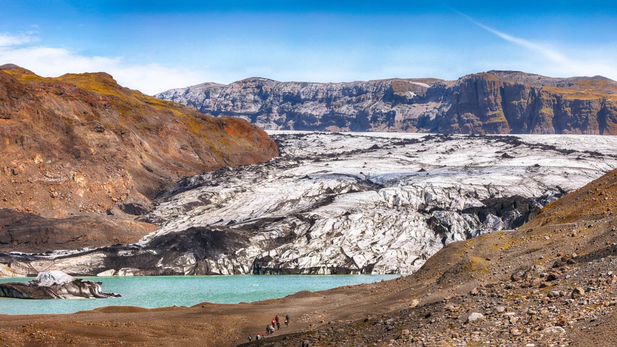 A glacier tongue spilling down between rocky slopes into a turquoise meltwater lagoon