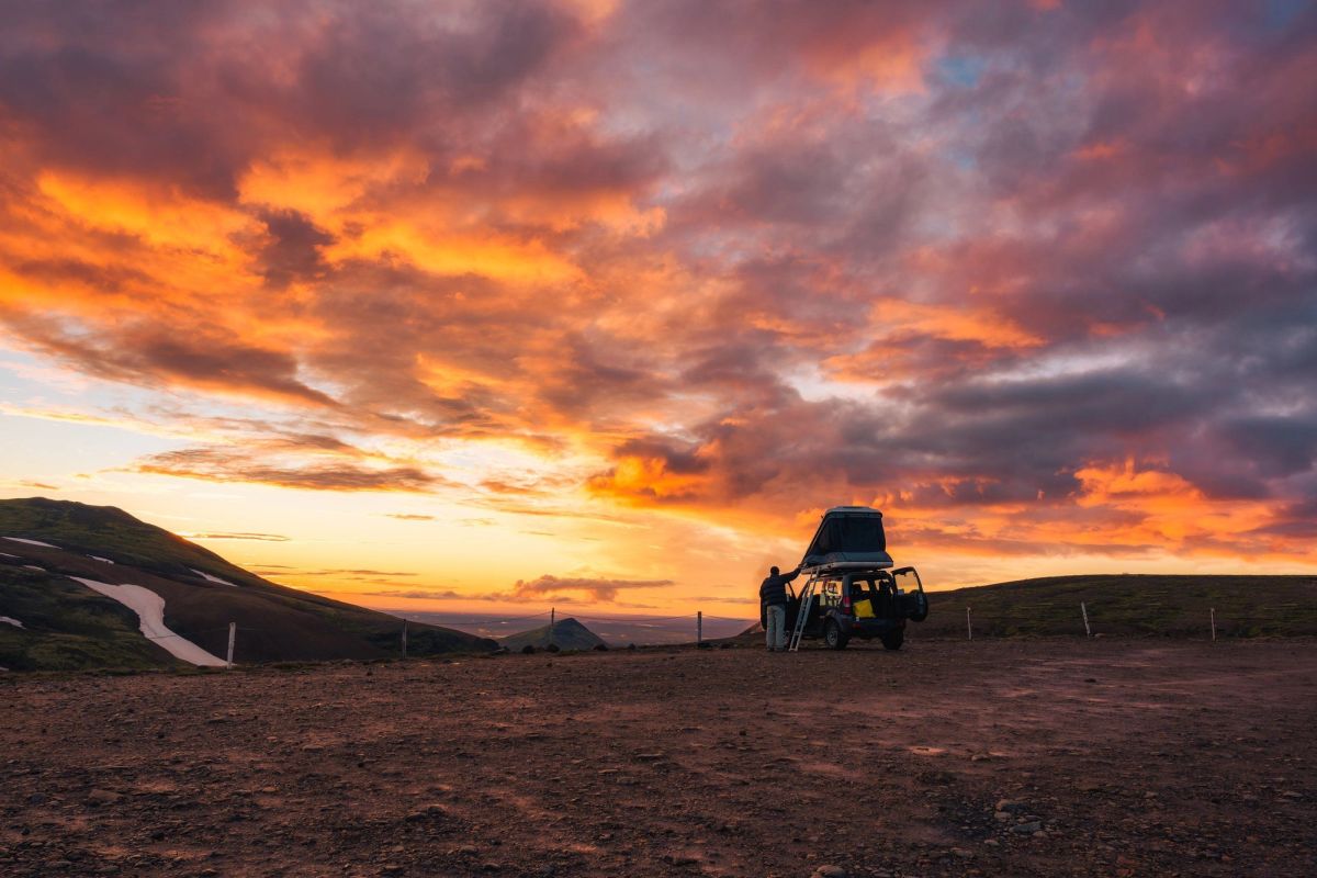 A 4x4 with a rooftop tent parked on a hillside under a vivid orange evening sky
