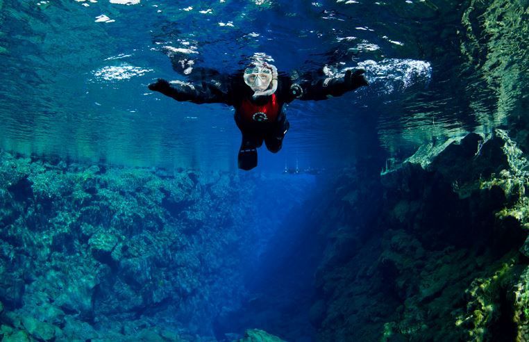 A snorkeller in the crystal-clear water of the Silfra fissure with rock walls below