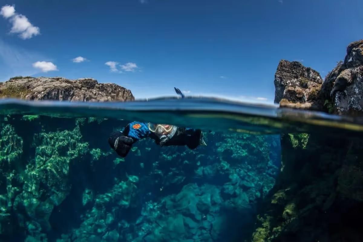 A snorkeller photographed half above and half below the surface at Silfra
