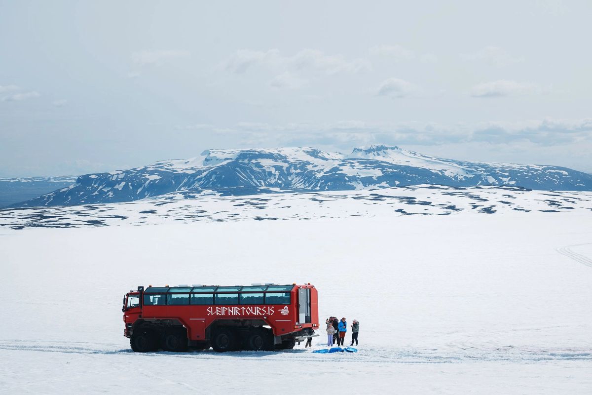 A super jeep parked on the glacier with people beside it