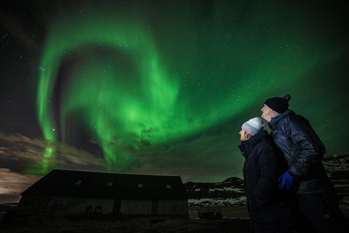 The northern lights over a barn with a couple watching