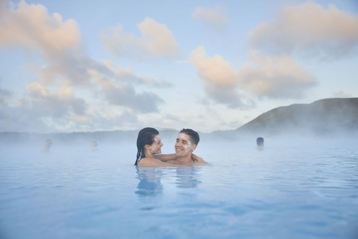 A couple embracing in the milky blue water of the Blue Lagoon, with steam rising around them