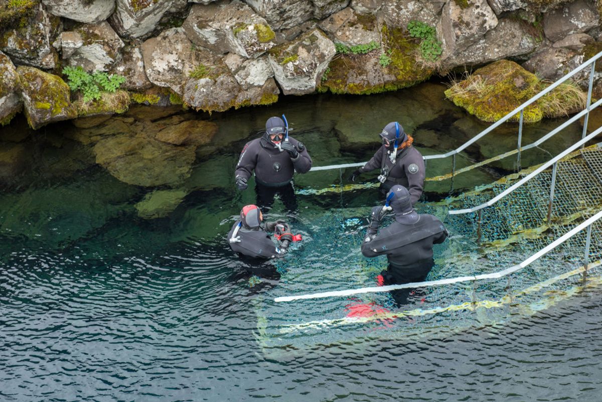 Scuba divers preparing entering in the water at Silfra rift, the place where Eurasian and the American tectonic plate are divided in Thingvellir National Park