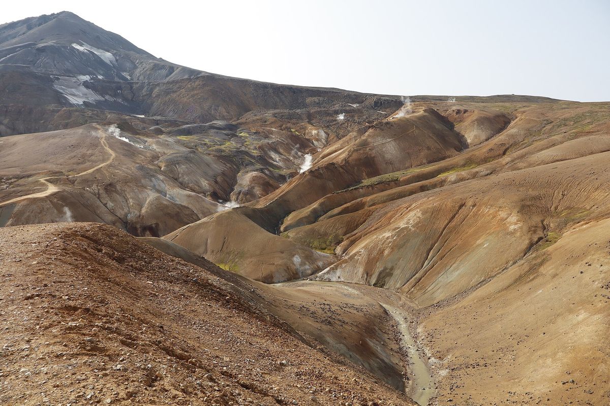 A gravel path winding between bare orange and grey slopes towards a snow-streaked peak
