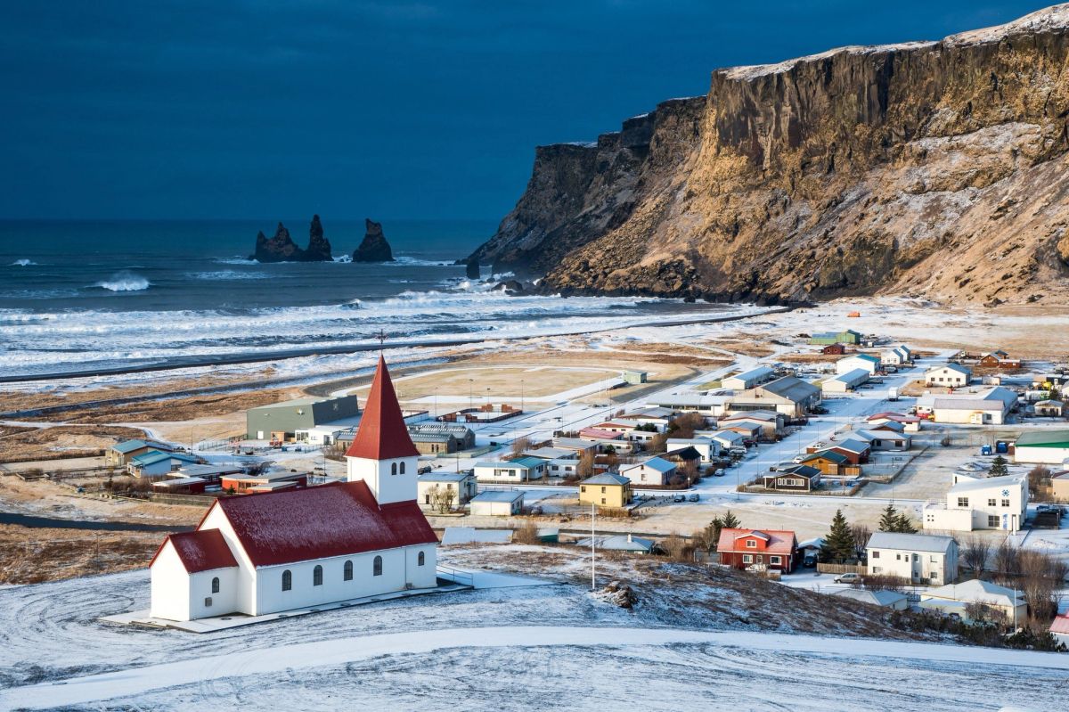 The red-roofed church of Vík above the snow-covered village, with sea stacks offshore