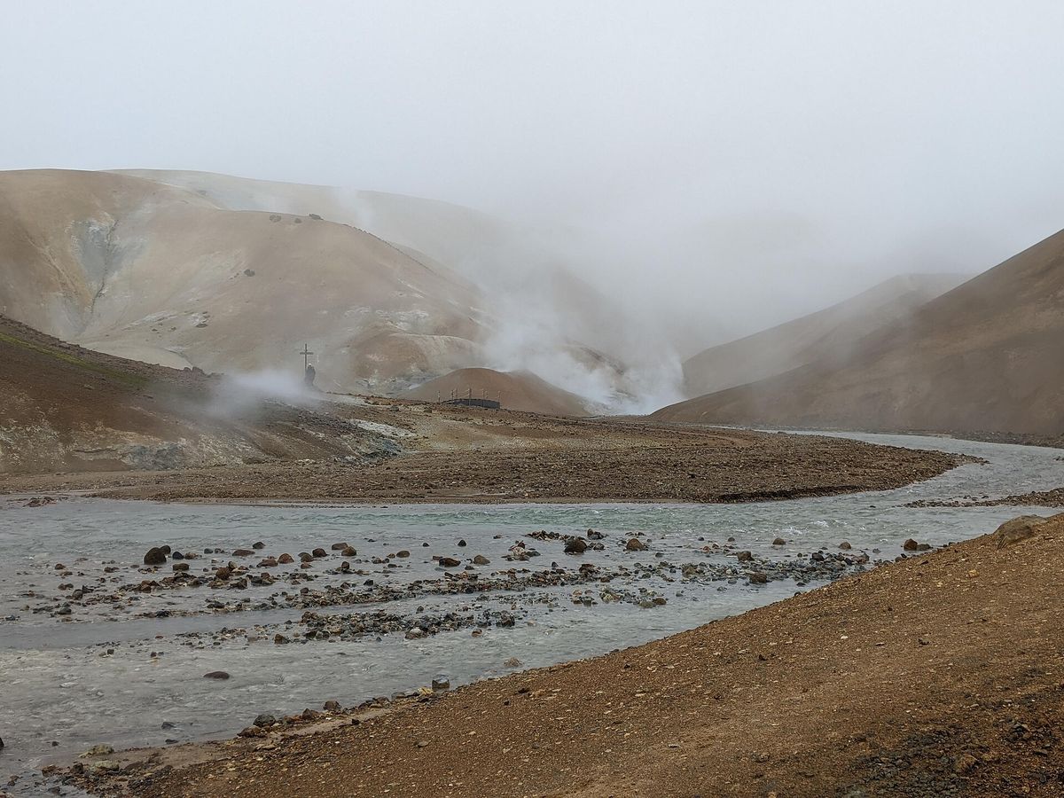 A river running through a grey valley, with steam drifting from hot springs on the hillsides