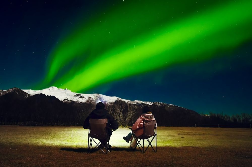 A couple sitting in camping chairs watching the northern lights