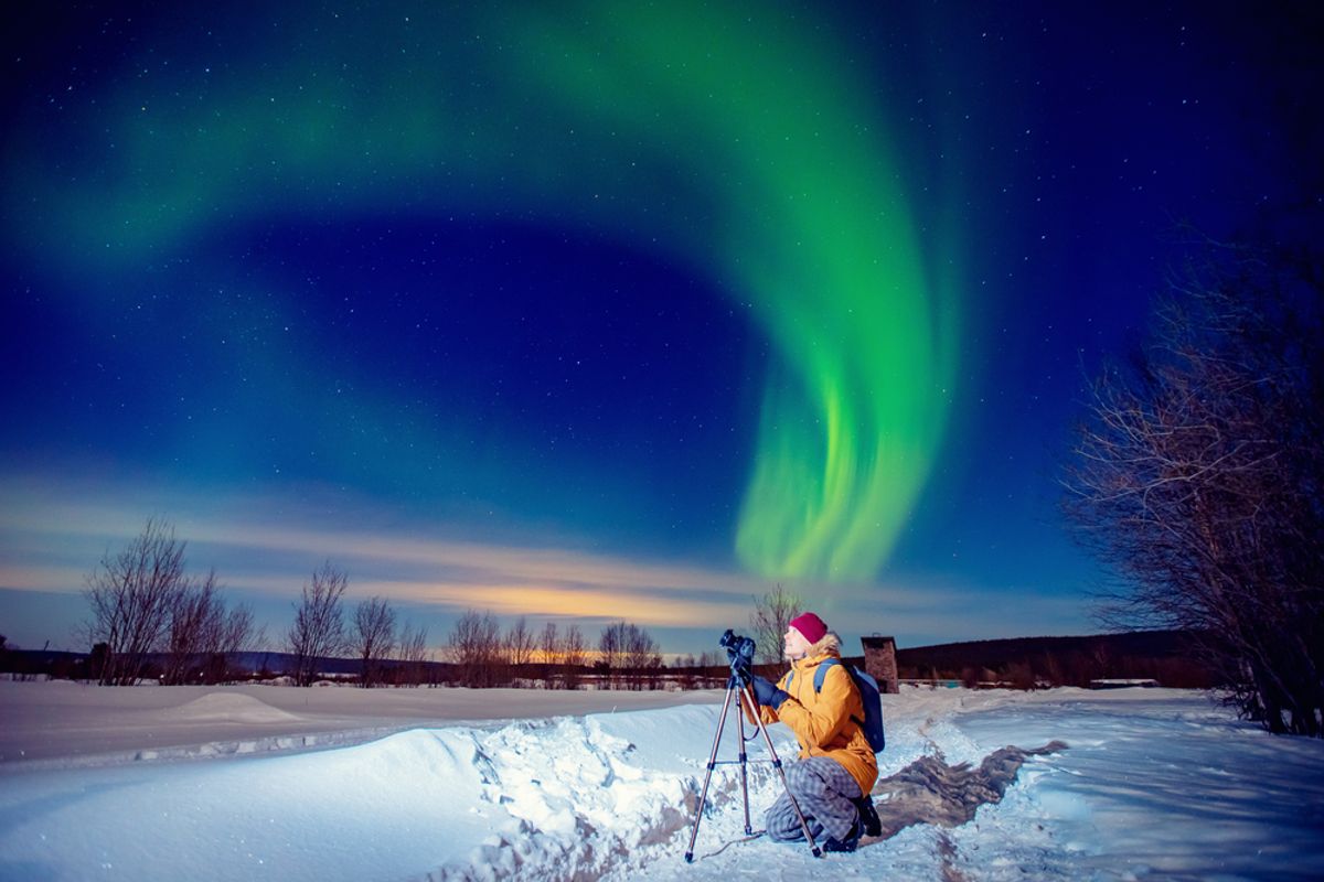 A photographer with a camera and tripod capturing the green aurora borealis in the night sky