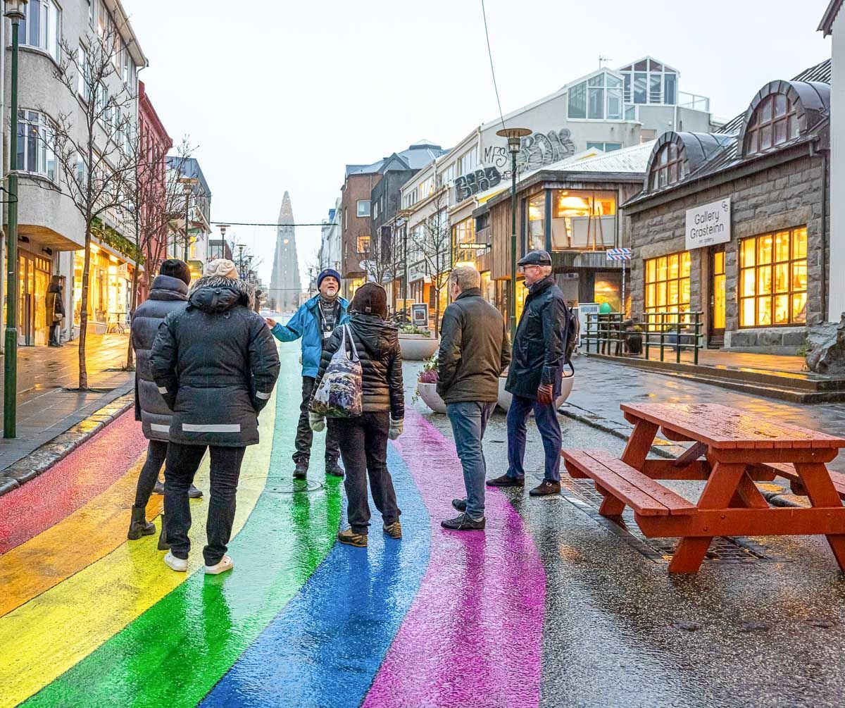 Visitors standing on a rainbow-painted street in Reykjavík, with Hallgrímskirkja church at the far end