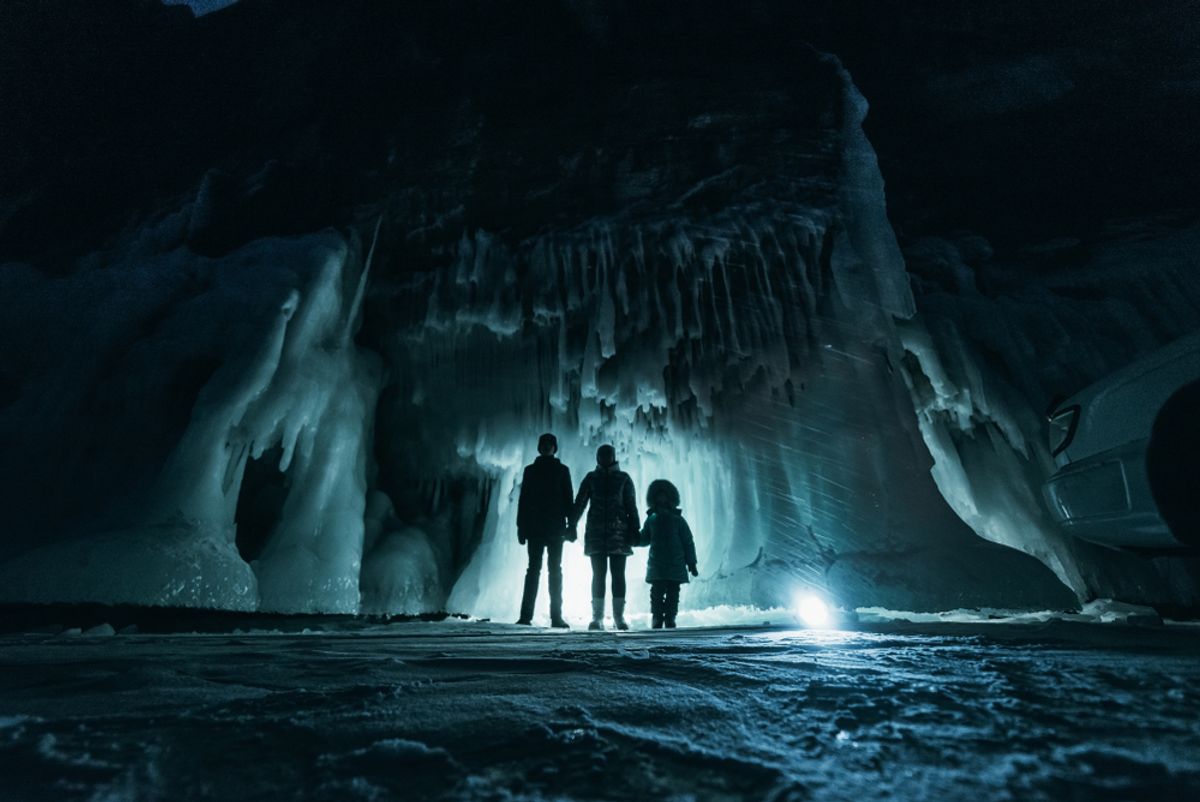 People exploring a surreal ice grotto cave, surrounded by a dark, majestic frozen landscape with glowing illuminated ice