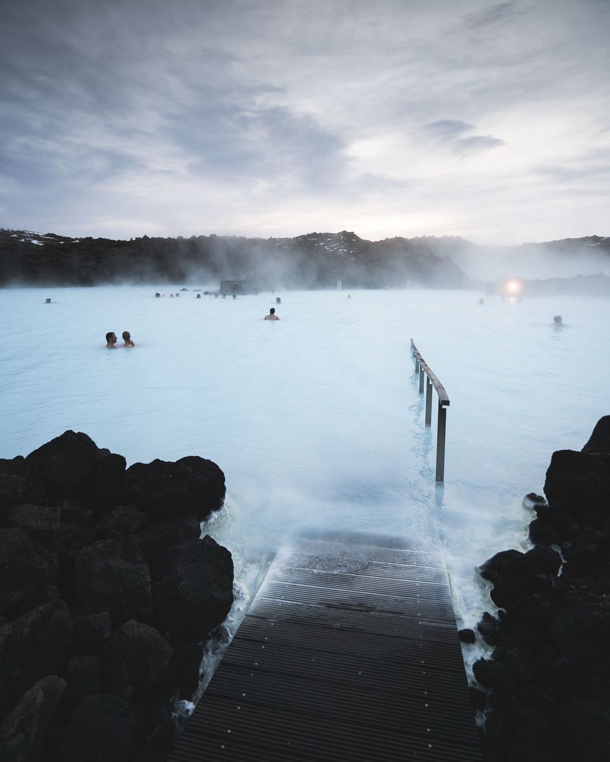Bathers in the milky blue water of the Blue Lagoon at dusk