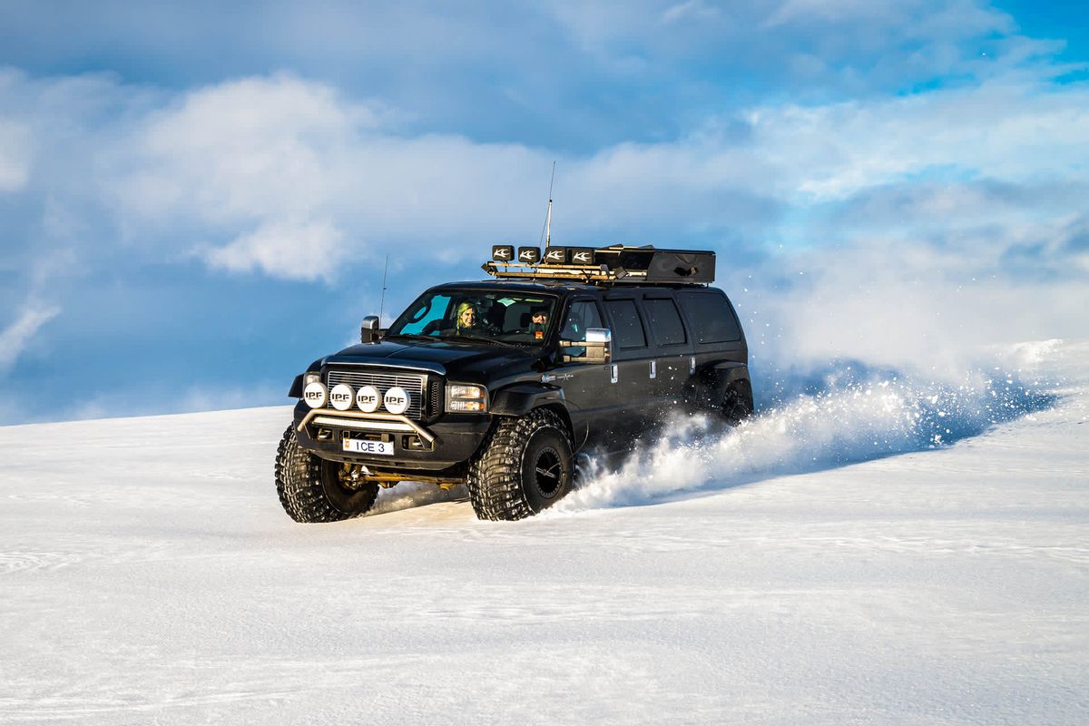 A monster truck with oversized tyres driving across glacier snow