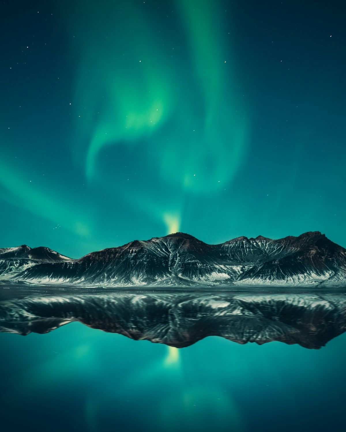 The aurora reflected over mountains in still water