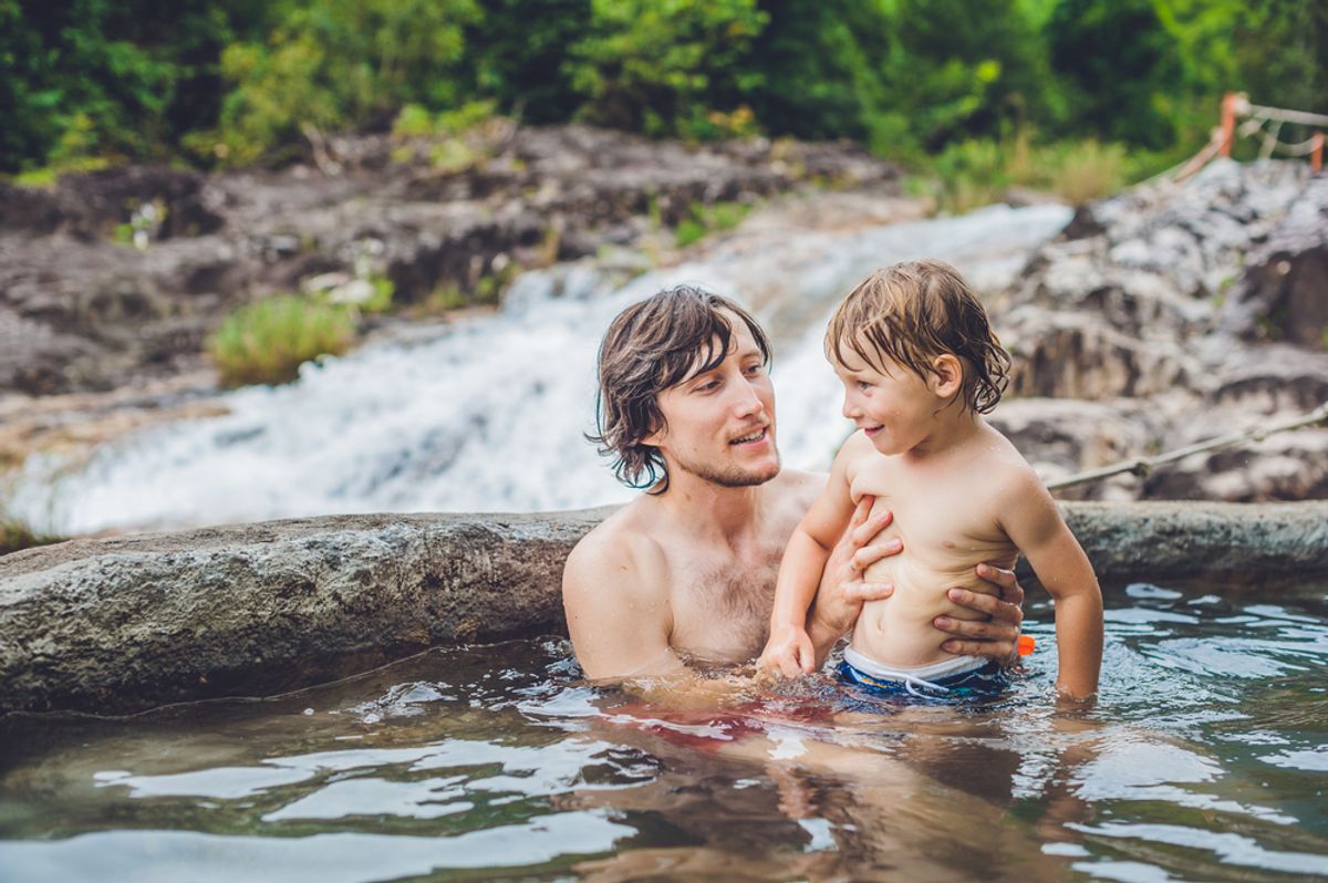 Father and son relaxing in a geothermal hot spring pool with a waterfall in the background