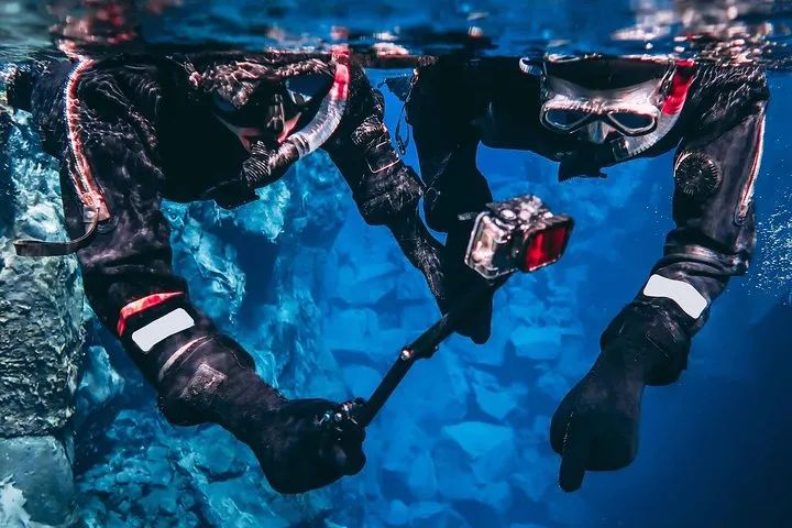 Snorkelers in dry suits adjusting thermal layers before entering the cold water at Silfra