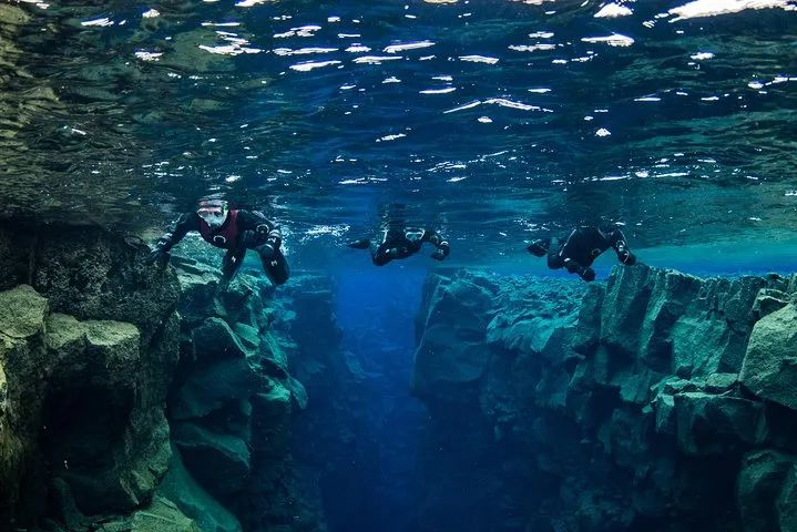 Guided snorkeling group swimming through the Silfra fissure between the tectonic plates