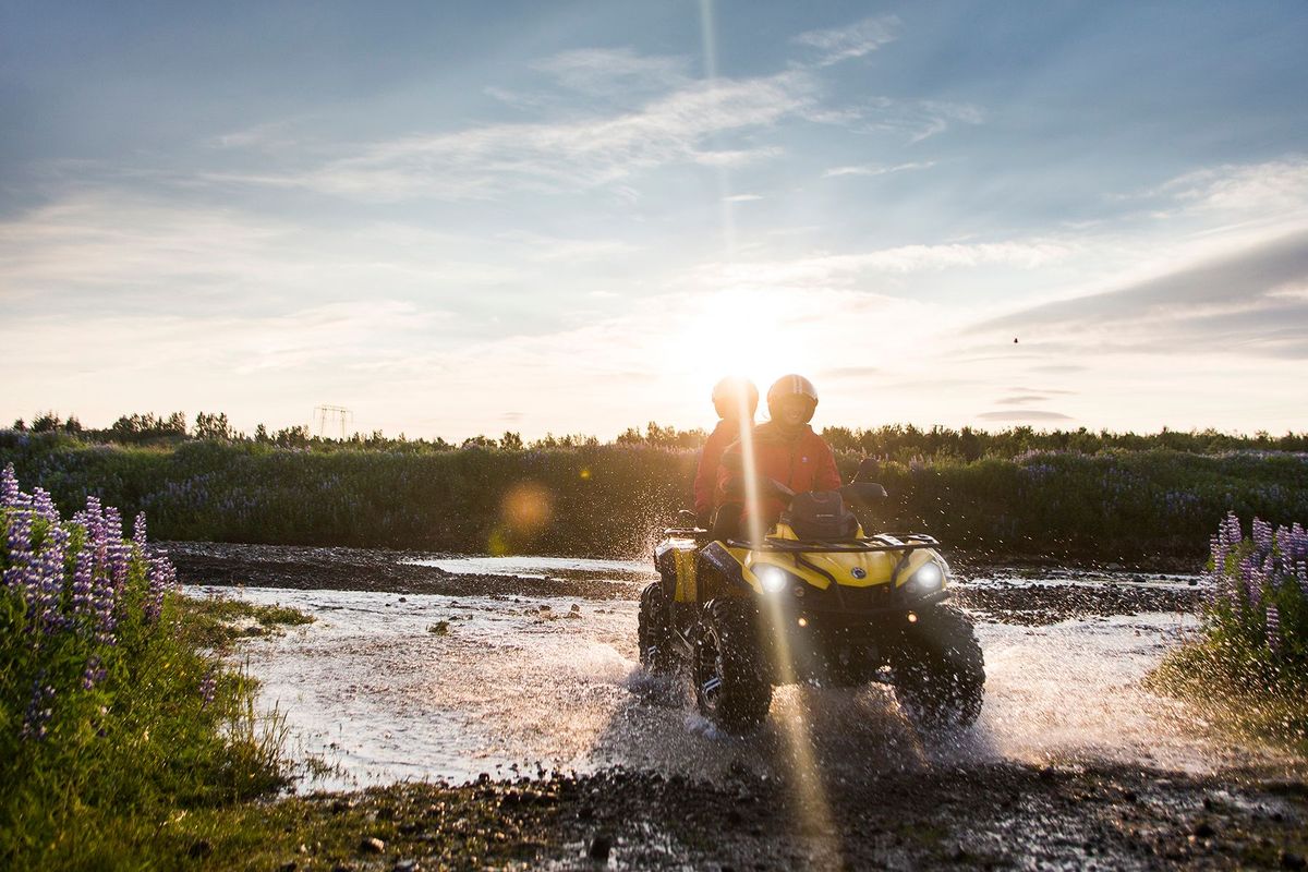 An ATV riding through shallow water at sunset