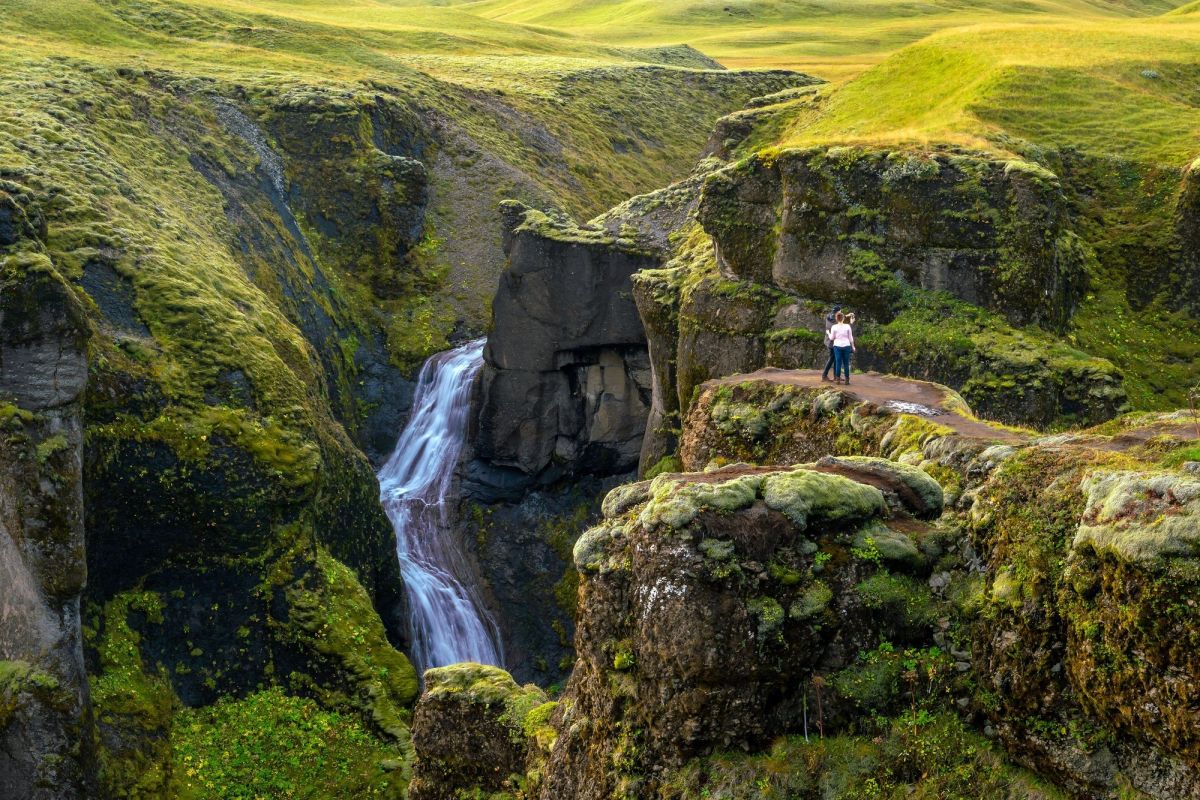 A narrow green canyon with steep mossy walls and a river winding along the bottom