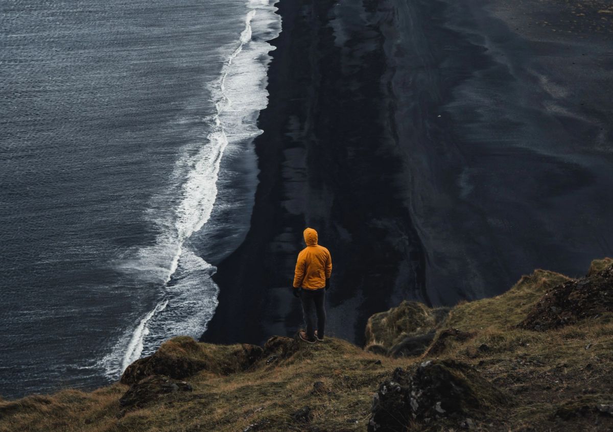 Waves on a black sand beach with a hiker on the cliff