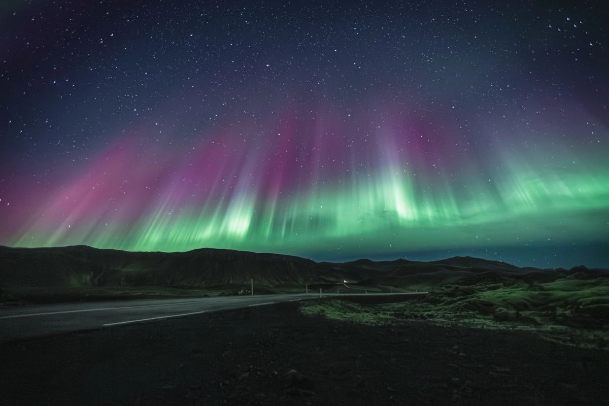 A pink and green aurora over a road in Iceland