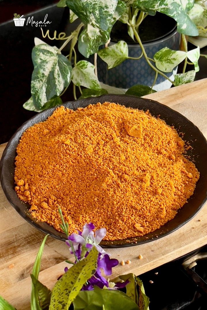 Idli milagai podi, a coarse orange spice powder, in a black bowl