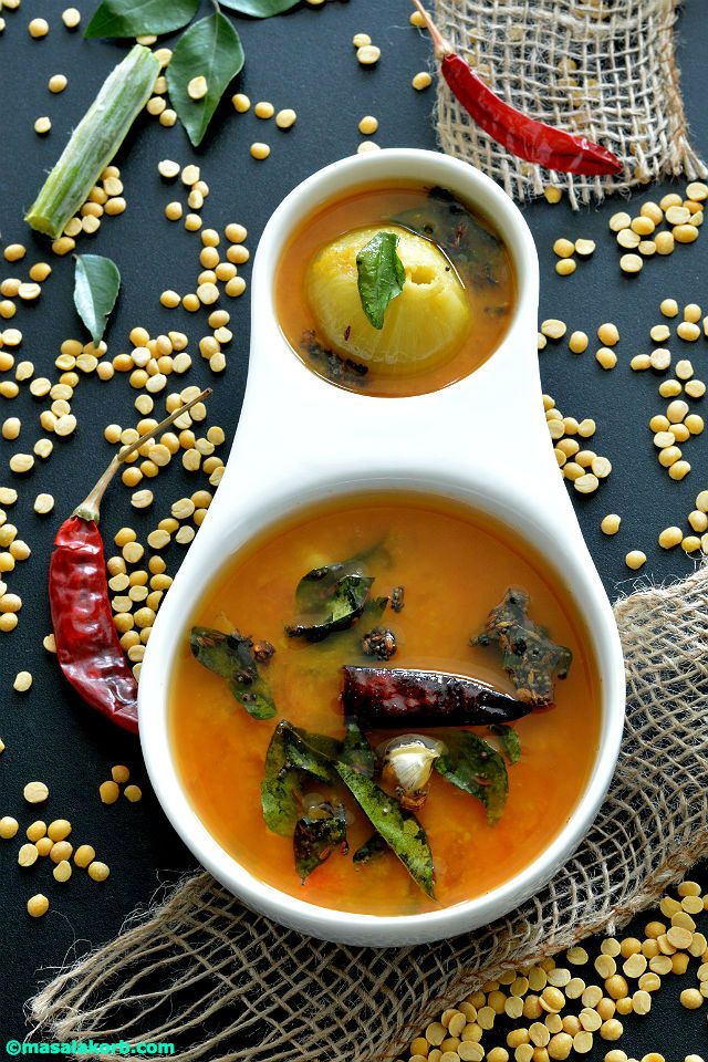 Pappu charu with curry leaves and a dry red chilli in a white bowl, toor dal scattered around