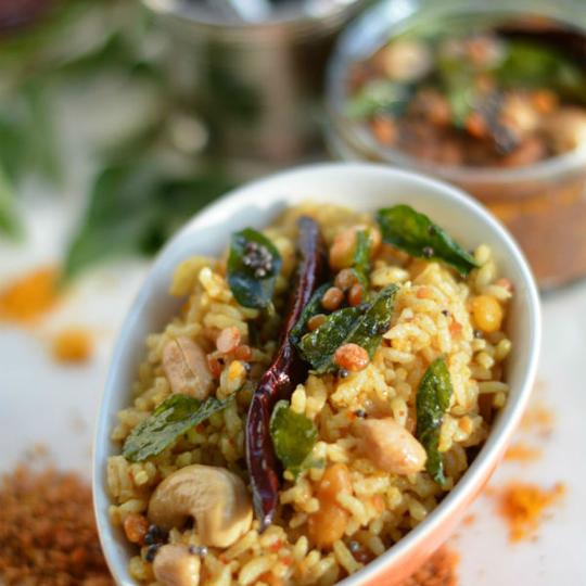 Tamarind rice with peanuts, cashews, a dry red chilli and curry leaves in a white bowl