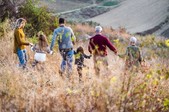 Fire voksne og to barn som holder hender med ryggen til mens de går gjennom et høstlig landskap