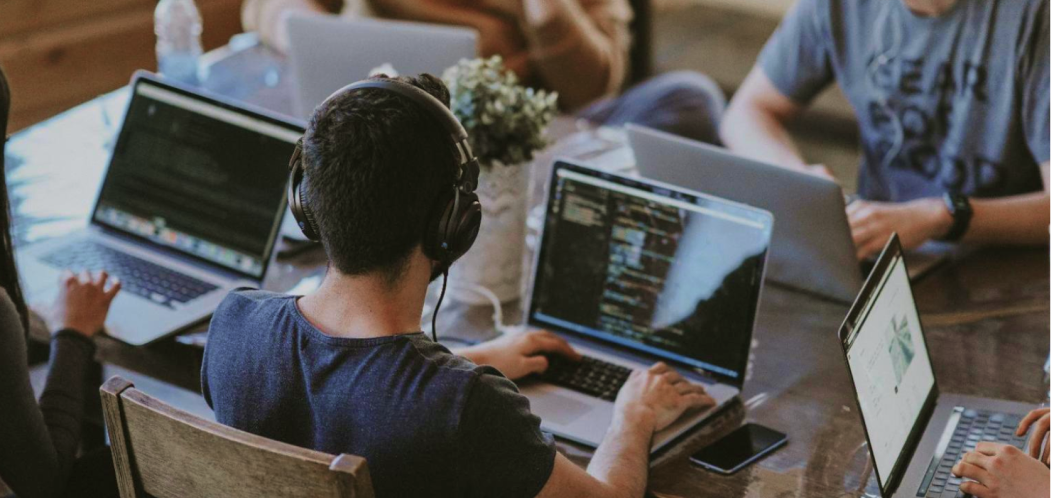 People sitting at a desk with typing with their laptops