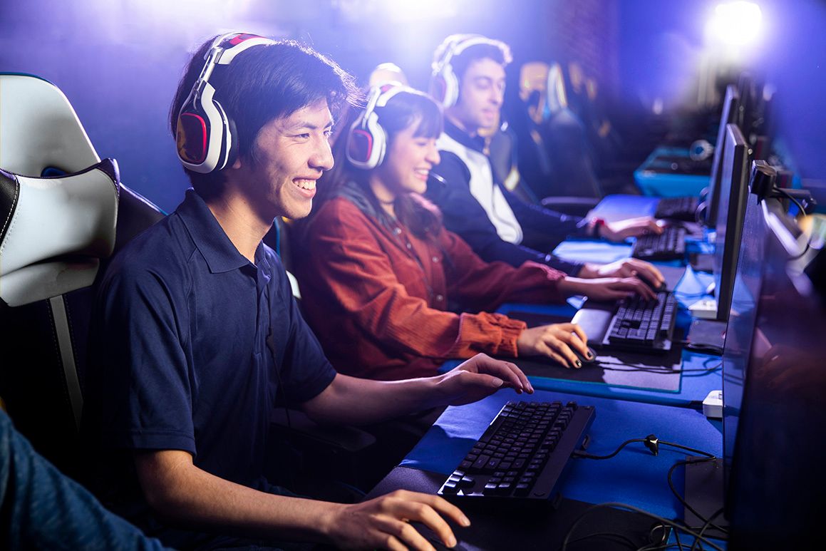 Three people sitting on gaming chairs, using their computer's mouse and keyboards, wearing headphones.